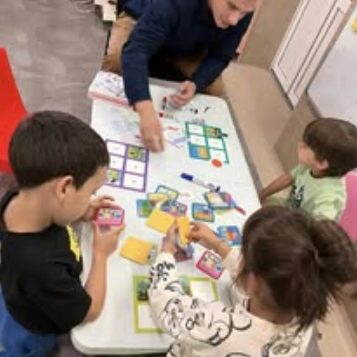 Copii lucrând la masă, cu cartonașe colorate, într-un atelier Kairos